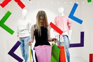 chica con bolsas de compras en el centro comercial contra maniquíes en el escaparate. foto