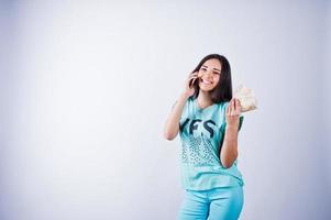 retrato de una chica atractiva con pantalones azul o turquesa y pantalones posando con mucho dinero y smartphone en las manos. foto