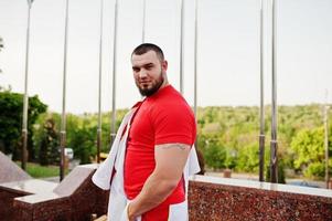 joven musculoso barbudo brutal vestido con traje deportivo blanco con camisa roja. foto