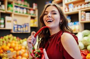 Girl in red holding hot chili peppers on fruits store. photo