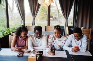 felices amigos africanos sentados y charlando en el café. grupo de personas negras reunidas en un restaurante y miran su teléfono móvil. foto