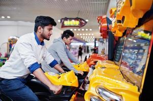 Two asian guys compete on speed rider arcade game motorcycle racing simulator machine. photo
