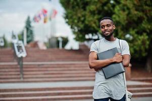 African student male posed with backpack and school items on yard of university, against flags of different countries. photo