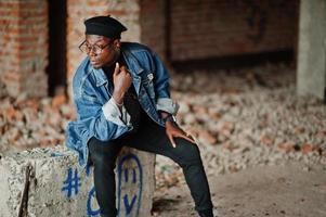 hombre afroamericano con chaqueta de jeans, boina y anteojos en una fábrica de ladrillos abandonada. foto