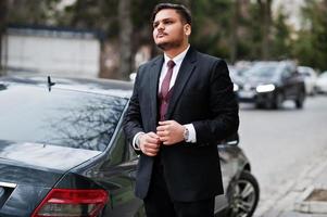 Stylish indian businessman in formal wear standing against black business car on street of city. photo