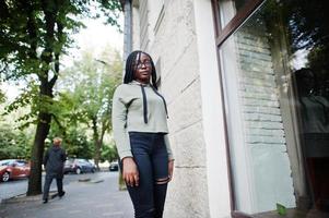 City portrait of positive young dark skinned female wearing green hoody and eyeglasses. photo