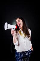 Portrait of a young woman in blue trousers and white blouse posing with megaphone in the studio. photo