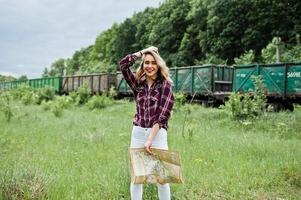 retrato de una joven rubia con camisa de tartán al lado del tren con un mapa. foto