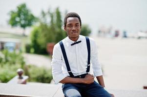 elegante hombre de negocios afroamericano en pantalones con tirantes y camisa con pajarita, posó al aire libre. foto