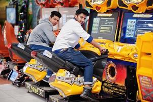 Two asian guys compete on speed rider arcade game motorcycle racing simulator machine. photo