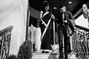 Lovely indian couple in love, wear at saree and elegant suit, posed outdoor terrace on summer sunny day, walking downstairs and hold hands together. photo