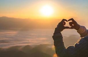 Woman making heart shape during sun rise, God is love concept, Heart shape, Mountain tourism,  The manifestation of love,  Love and feelings. photo