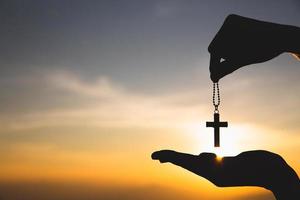 silueta de mano sosteniendo collar crucifijo fondo amanecer. concepto de cristiano, cristianismo, religión católica, dios. foto