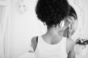 joven afroamericana mirando el espejo y escuchando música en los auriculares. foto