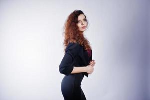 Brunette curly haired girl in black office jacket with skirt, on bra at studio against white background. Sexy businesswoman. photo