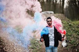 Street style arab man in eyeglasses hold hand flare with red and blue smoke grenade bomb. photo