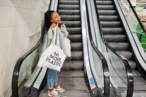 African woman with shopping eco bags on escalator at mall. photo