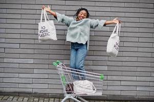 no más plástico. mujer africana con carro de compras y bolsas ecológicas salta al mercado al aire libre. foto