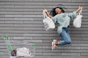 No more plastic. African woman with shopping cart trolley and eco bags jump outdoor market. photo