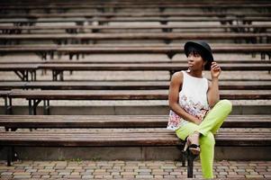 increíble mujer modelo afroamericana en pantalones verdes y sombrero negro posó en el banco. foto