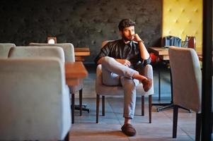 Confident young indian man in black shirt sitting at cafe. photo