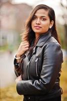 primer plano retrato de una linda chica india con vestido negro de sari y chaqueta de cuero posada al aire libre en la calle de otoño. foto