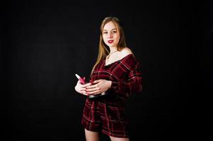 Young housewife in checkered dress with saucepan and kitchen spoon isolated on black background. photo