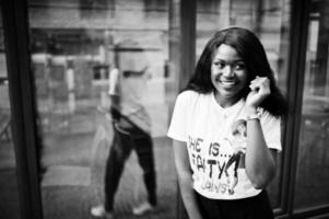 elegante mujer afroamericana en camiseta impresa posada al aire libre contra la ventana. foto