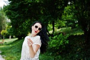 Brunette girl in green skirt and white blouse with sunglasses posed at park. photo