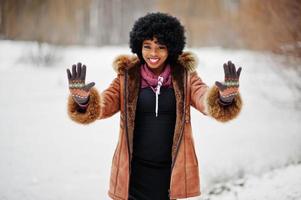 mujer afroamericana de pelo rizado con abrigo de piel de oveja y guantes posados en el día de invierno, muestra dos manos. foto