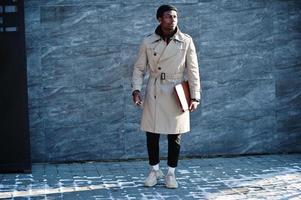 Handsome african american man posing outside in black hat and beige coat with folder in hand. photo