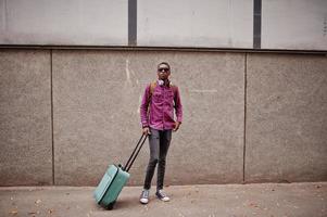 African american man in checkered shirt, sunglasses and earphones with suitcase. Black man traveler. photo