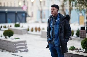 el hombre africano usa una chaqueta en el clima frío del invierno posado al aire libre con auriculares en las orejas. foto