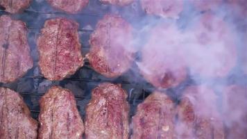 Barbeque footage shows a beautiful day in the garden where a barbecue grill is set up. Meat slices fill the grill and smoke slowly comes up from the grill and spreads. Use this to establish an outdoor video