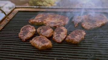 Barbeque footage shows a beautiful day in the garden where a barbecue grill is set up. Meat slices fill the grill and smoke slowly comes up from the grill and spreads. Use this to establish an outdoor video