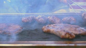 Barbeque footage shows a beautiful day in the garden where a barbecue grill is set up. Meat slices fill the grill and smoke slowly comes up from the grill and spreads. Use this to establish an outdoor video