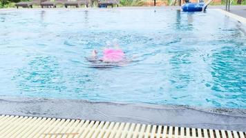 una niña feliz está nadando y jugando en la piscina al aire libre en un resort tropical durante las vacaciones familiares de verano. niña aprendiendo a bucear y nadar. video