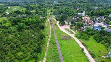 imagens de drone de um trem de passageiros de locomotiva a diesel em uma ferrovia rural movendo-se por uma floresta tropical exuberante. imagens aéreas do trem em execução pela bela paisagem na tailândia. video