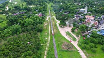 riprese con drone di un treno passeggeri di una locomotiva diesel su un binario ferroviario rurale che si muove attraverso una lussureggiante foresta tropicale. riprese aeree del treno in corsa attraverso il bellissimo paesaggio in Thailandia. video