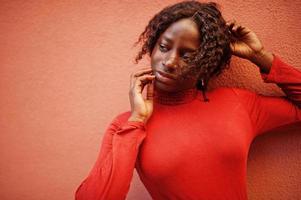 retrato de una mujer africana de pelo rizado con cuello alto rojo de moda posando contra una pared de rosas. foto