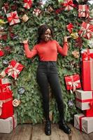 Portrait of a curly haired african woman wearing fashionable red turtleneck posing against christmas decorations, new year eve theme. photo