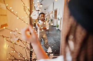 mujer afroamericana en overoles y boina contra el espejo en una habitación de luz suave. foto