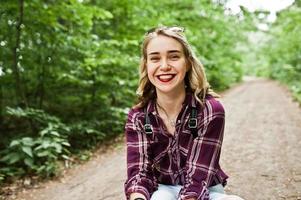 Portrait of a beautiful blond girl in tartan shirt sitting on the ground in the countryside. photo