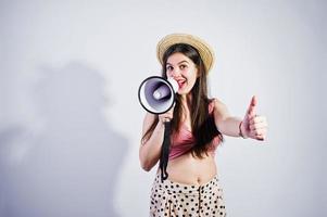 retrato de una hermosa joven en traje de baño y sombrero habla por megáfono en el estudio. foto