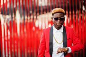 Fashion african american man model at red suit, with highlights hair and handbag posed at street and looking at his watches. photo