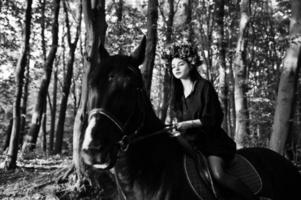 chica mística en ropa de corona en negro a caballo en madera. foto