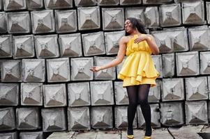 elegante mujer afroamericana con vestido amarillo posada sobre fondo de textura de piedra. foto