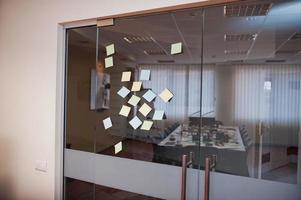 Blank colored sticky note or post note stuck on glass wall at office. photo