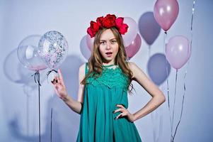 Happy girl in green turqoise dress and wreath with colored balloons isolated on white. Celebrating birthday theme. photo