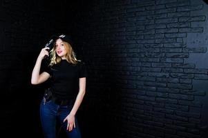 FBI female agent in cap and with gun at studio against dark brick wall. photo